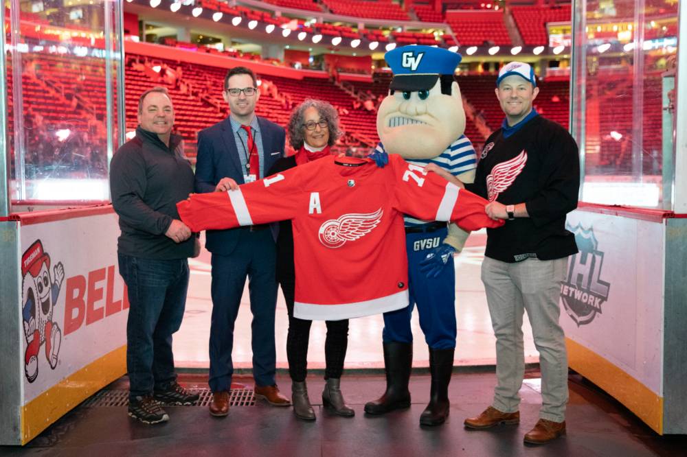 Alumni pose with Louie the Laker while holding up a Red Wings Jersey at the Detroit Red Wings GVSU Night